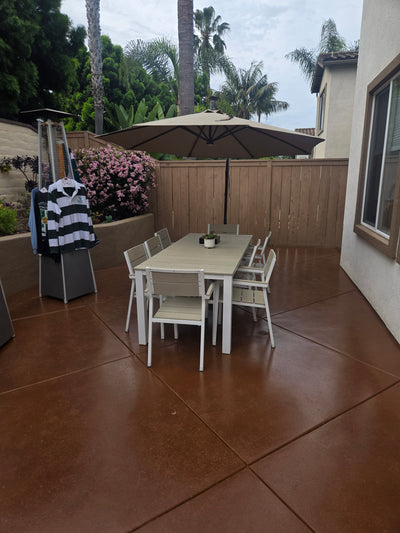 Real patio project using Smith's Color Floor stain in Dark Adobe; deep reddish-brown concrete beneath a dining table.